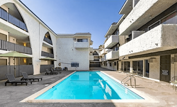 A swimming pool is surrounded by lounge chairs and is located between two buildings.